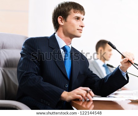 Portrait of a businessman, said into the microphone, in the background colleagues communicate with each other