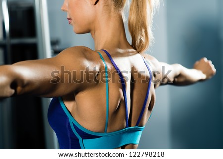 female athlete straining back muscles and arms, do sport in the fitness club