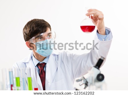 scientist working in the lab, in protective mask, examines a test tube with liquid