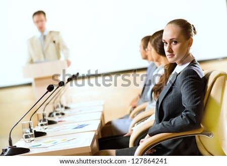 group of business people sitting at the tables at the presentation, woman looking at the camera