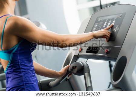 woman adjusts the treadmill at the beginning of training, do fitness in the sport club