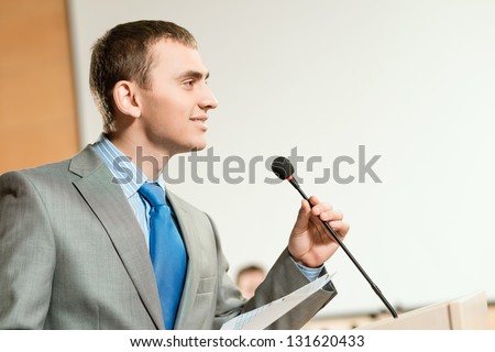 Portrait of a business man holding microphone on conference, speaks into the microphone and looks into the room