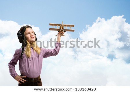 girl in helmet pilot playing with a toy wooden airplane in the clouds, dreaming of becoming a pilot