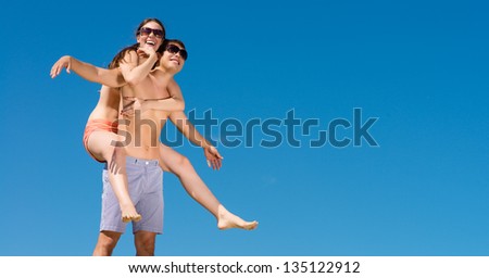girl sitting on a guy having fun and waving their arms, behind blue sky