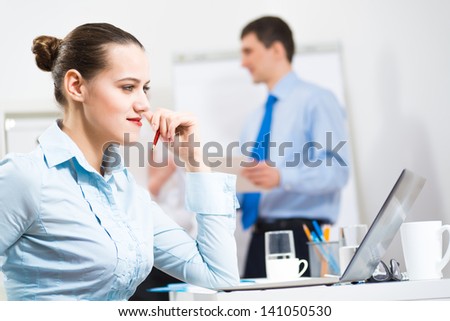 Business woman thinks for a laptop in the office, in the background debating colleagues