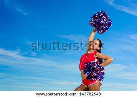 Young cheerleader in red costume with pampon against blue sky