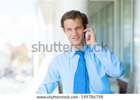 successful young businessman smiling, standing on the balcony and talking on cell phone