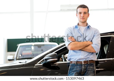 man standing near a car with his arms crossed, car showroom
