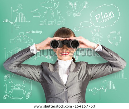 business woman looking through binoculars behind her wall with sketches