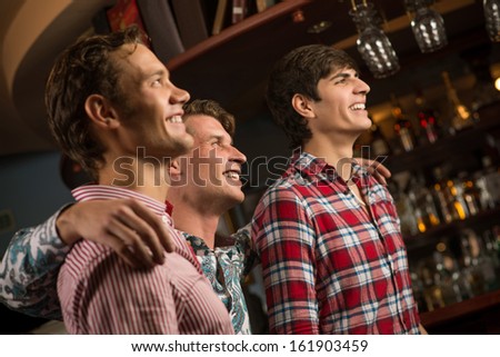 Three men stand in a row embracing smile and look in front of you, sports fans