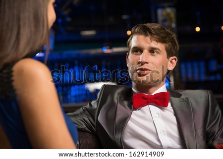 portrait of a man in a nightclub, sitting on the couch and talking with woman