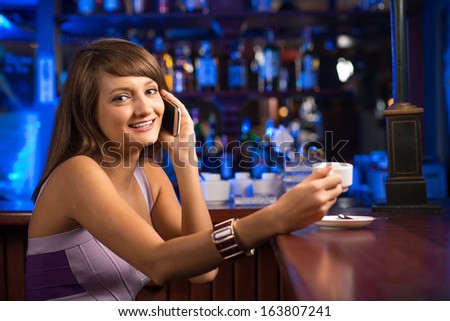 woman talking on the phone while sitting with a cup of coffee at the bar