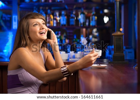 woman talking on the phone while sitting with a cup of coffee at the bar