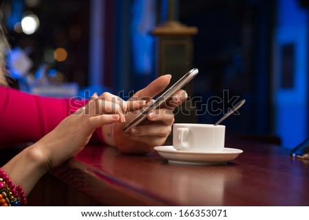 close-up of female hands holding a cell phone, sitting at the bar, next to a cup of coffee