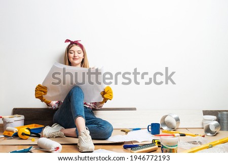 Happy girl sitting on floor with paper blueprint. Home remodeling after moving. Construction tools and materials for building. Young woman wearing checkered shirt and jeans redesigning her home. Foto stock © 
