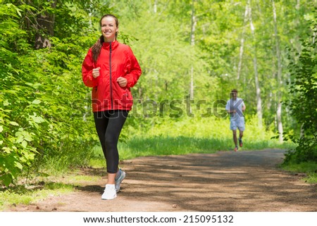 healthy young female athlete running in a summer park smiling and happy while working out