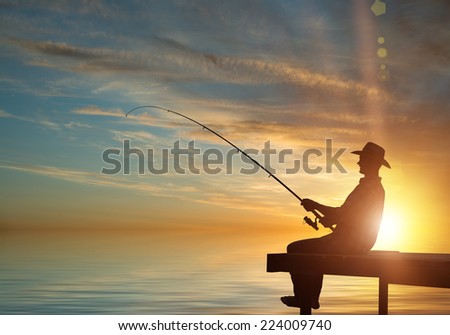 Silhouette of man sitting at bridge and fishing