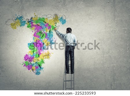 Back view of businessman standing on ladder and drawing on wall