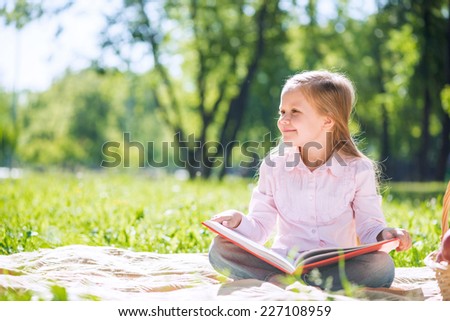 Adorable girl in summer park reading book