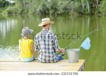 Back view of father and daughter sitting on pier and fishing