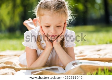 Little cute girl in summer park reading book
