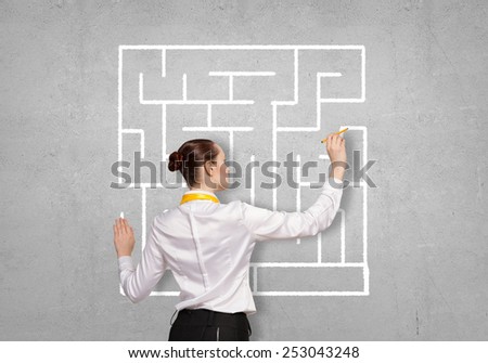 Back view of businesswoman drawing labyrinth on wall