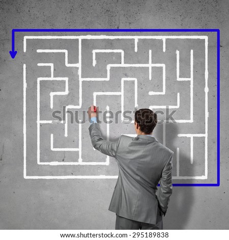 Back view of businessman drawing labyrinth on wall