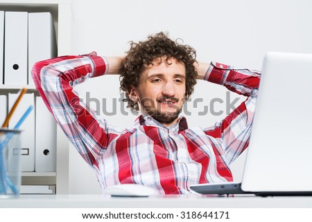 Young relaxed man in checked shirt in his office with hands on head