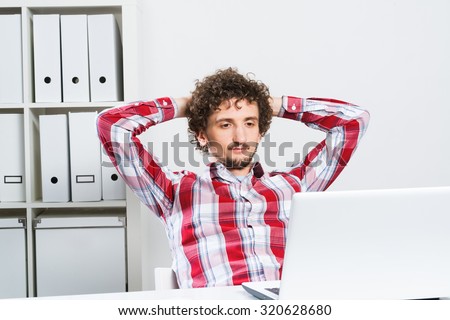 Young relaxed man in checked shirt in his office with hands on head