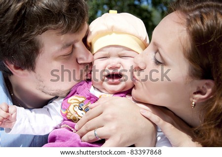 Father and mother kissing a child, the child is crying and sad
