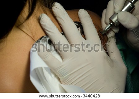 A man makes a butterfly-tatoo on the shoulder of a young girl. Attention on the