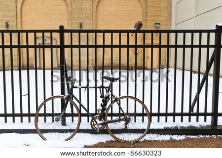Black bicycle leaning against black iron fence in winter