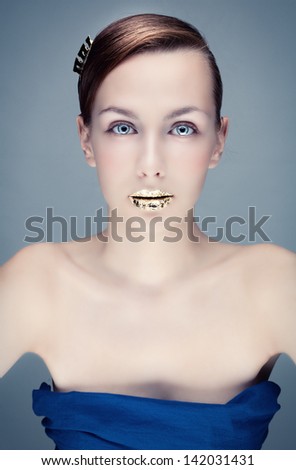 Studio photo of a young woman with bright make-up and gold lips.
