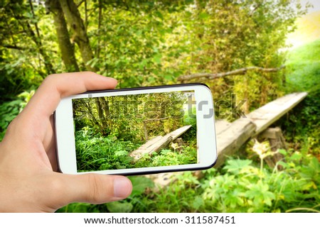 Hands taking photo landscape with a wooden bridge over a river  with smartphone.