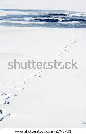 Vertical view of footprints in snow on frozen lake leading to patch of thin ice