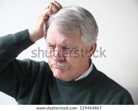 senior man with frustrated, puzzled expression scratches his head