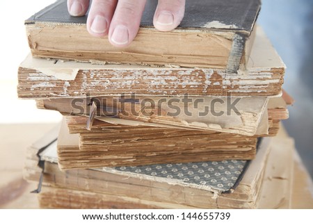 stack of old books with a man\'s fingers on top