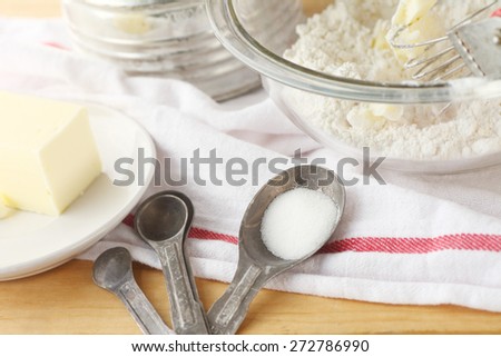 Mixing bowl with flour and butter, vintage sifter, measuring spoons and dish cloth