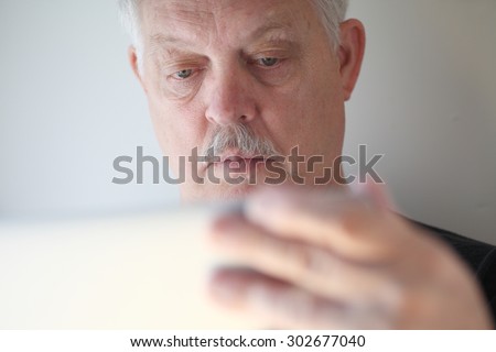 A senior man with a hand on his laptop cover checks his screen.