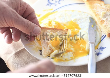 A man uses a piece of toast to scoop up some fried egg.