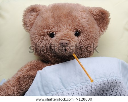ad teddy bear on a pale yellow pillow with a thermometer in its mouth and covered by a blue baby blanket