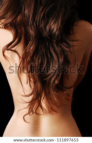 Nude female back is covered with dark tresses on the black background.