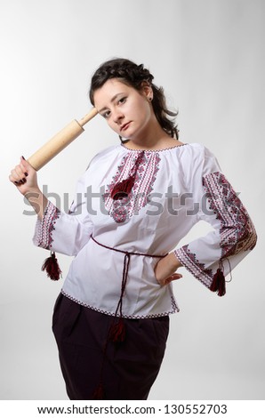 Cheerful young woman is holding a rolling pin. She is wearing a shirt embroidered and a skirt.