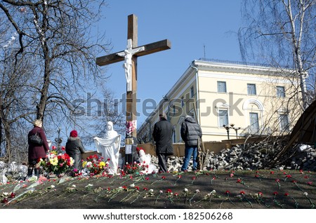 KYIV, UKRAINE - MARCH 09 2014: People pray near the Cross in the hill strewn with flowers. Ukrainian capital is sorrowing over victims of the shooting at the Independence square in February 2014.