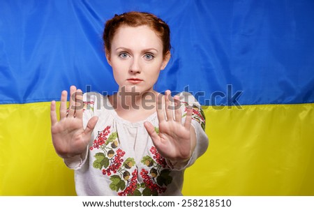 The frightened young woman is making a gesture of defense against the national Ukrainian flag. She is wearing a shirt embroidered.