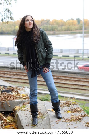 Teenage girl in wind-breaker and  jeans stands on river bank in\
\
autumn.
