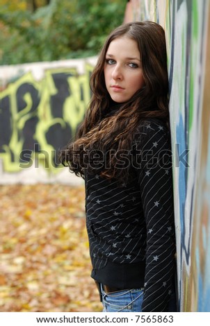 Teenage sad girl leans on graffiti wall.