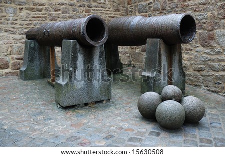 Old English cannons with stone balls on cobble pavement in the corner of boundary wall