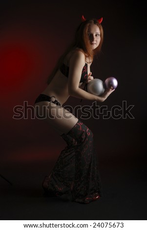 Perky young woman stealing christmas balls in the dark, stage costume of devil