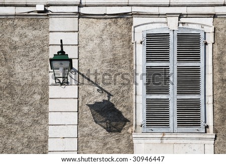 Dark shadow of lantern crawls on sunlit wall to window closed with shutters